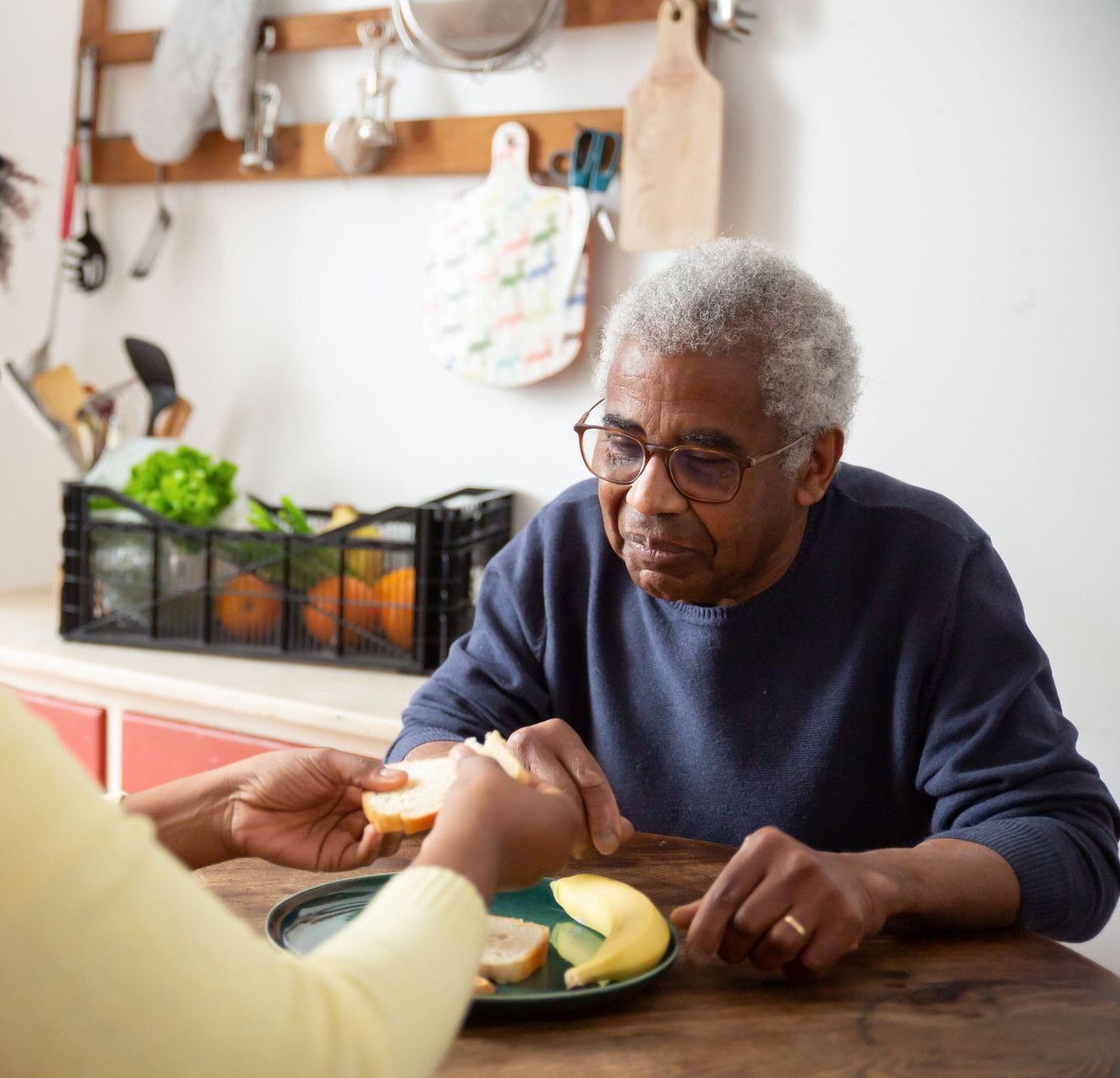 A woman assists an elderly man with meals at home, showcasing care and support.