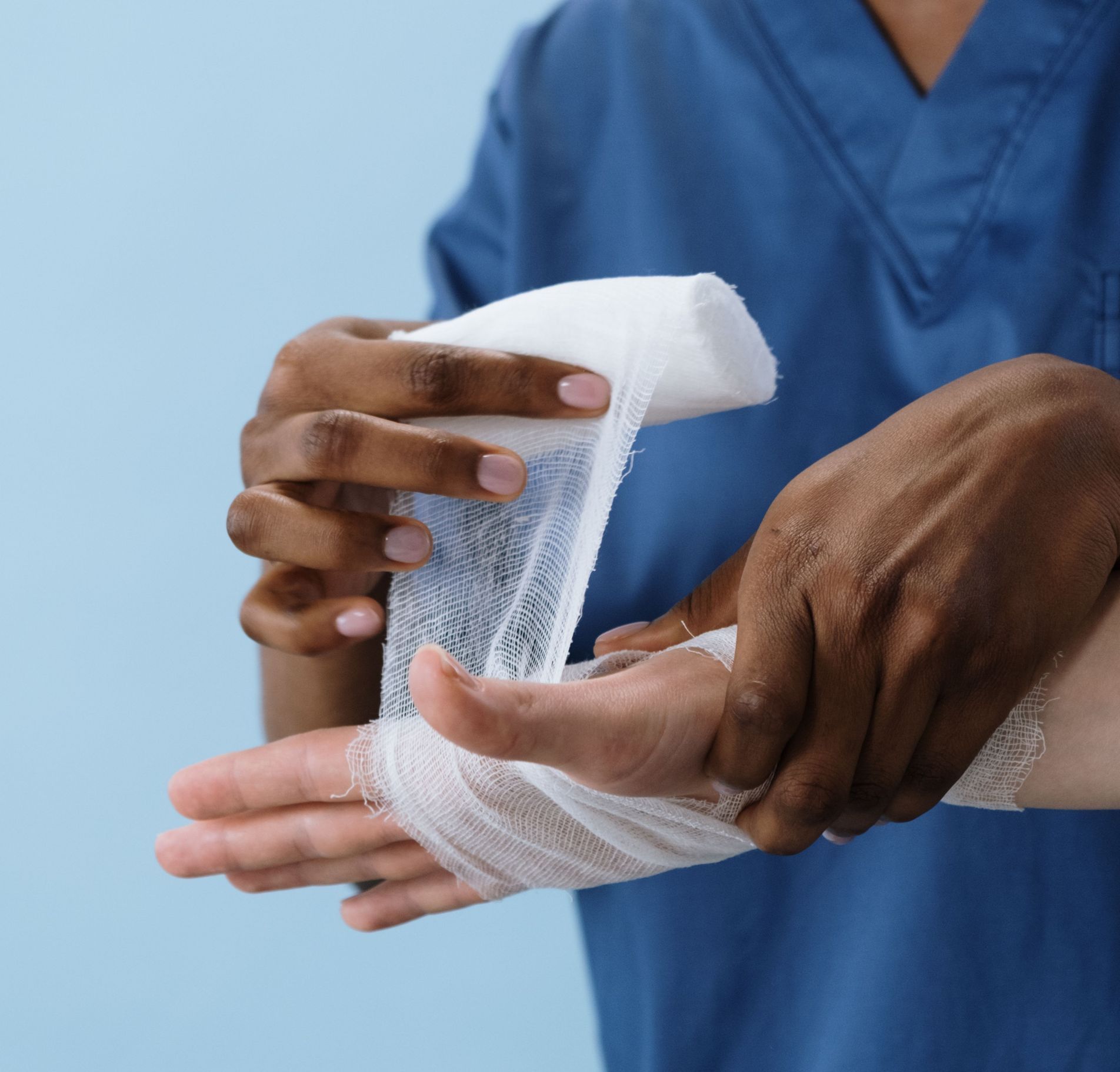 A healthcare professional wrapping a patient's hand with gauze for injury care.